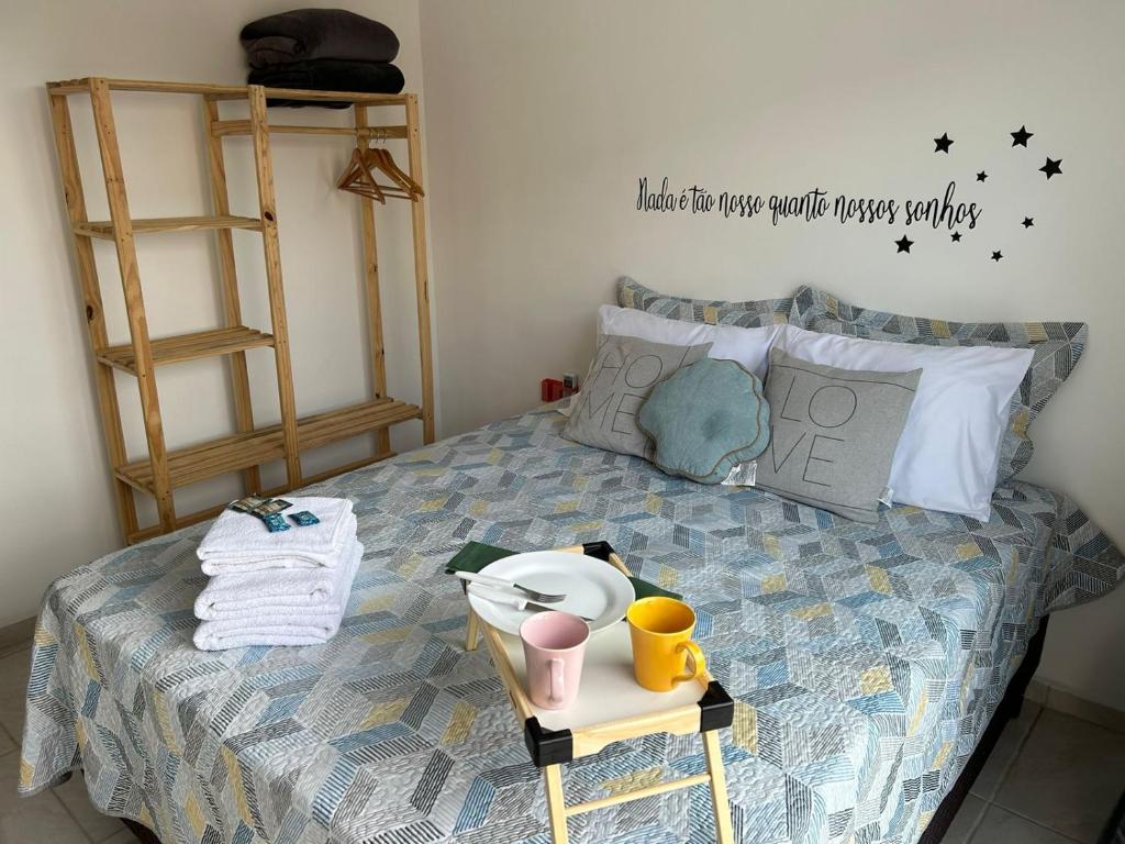 suíte do Bora Bora Residence com uma cama casal enfeitada por quatro travesseiros e três almofadas menores, sendo uma delas em formato de concha. Em cima da cama há ainda um conjunto de toalhas com sabonetes embalados e uma pequena bandeja com um prato e duas xícaras.