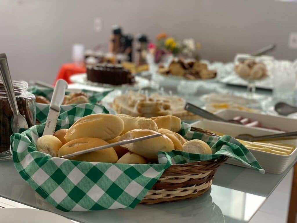 Café da manhã do Hotel Pousada Acauã Acesso através de escadas. Uma mesa com pães, bolos, bolachas e frios.