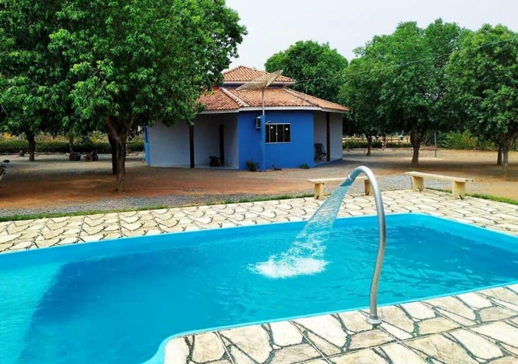 Piscina do Canto das Araras - Estivado Bom Jardim. Uma piscina na frente com uma castata. Do lado direito da piscina dois bancos. No fundo, árvores e um chalé,