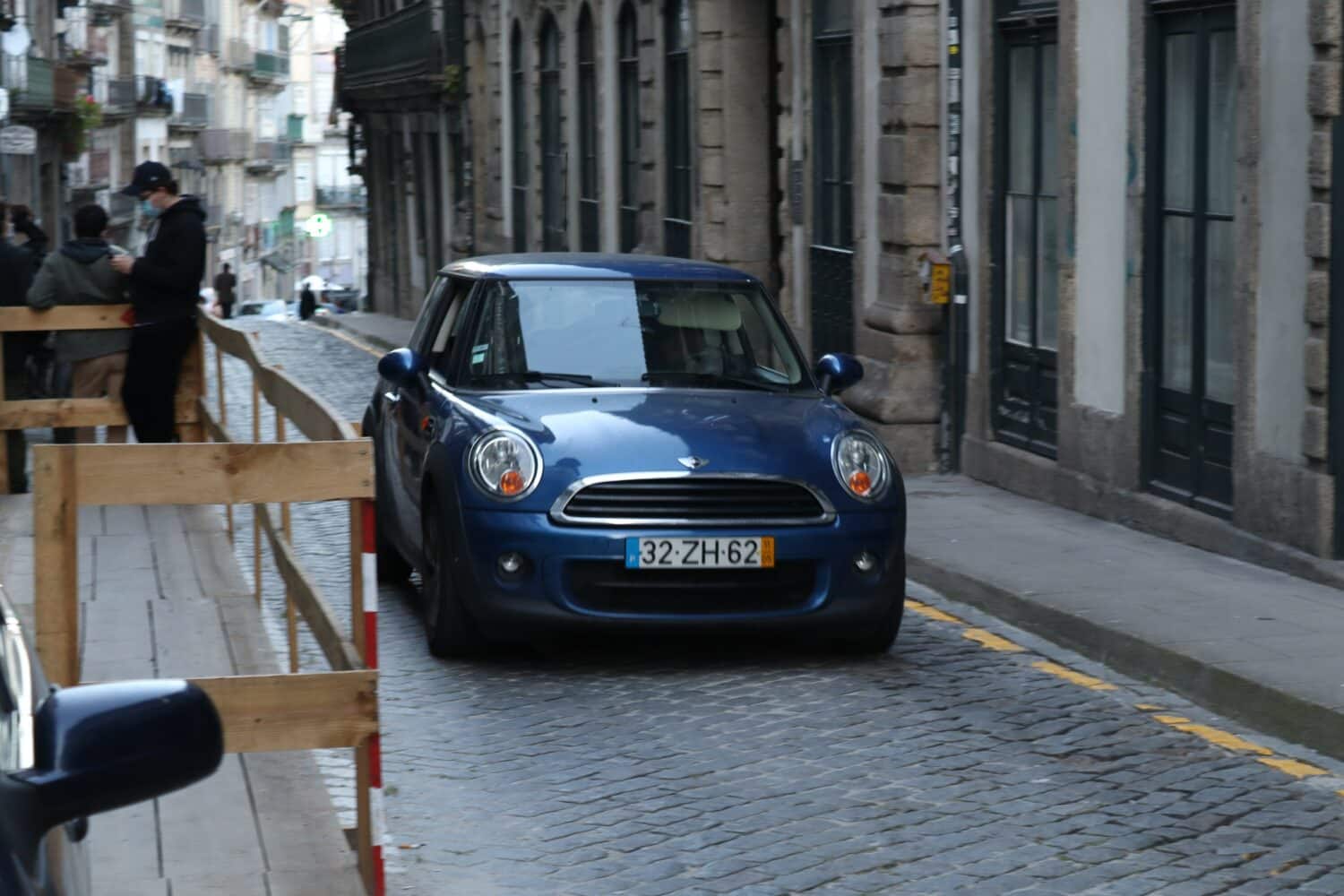 Carro azul escuro andando em uma ruela durante o dia. Representa aluguel de carros no Porto.
