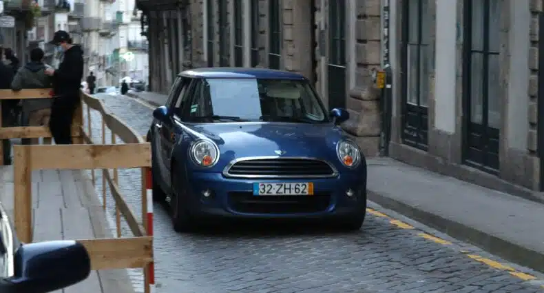 Carro azul escuro andando em uma ruela durante o dia. Representa aluguel de carros no Porto.
