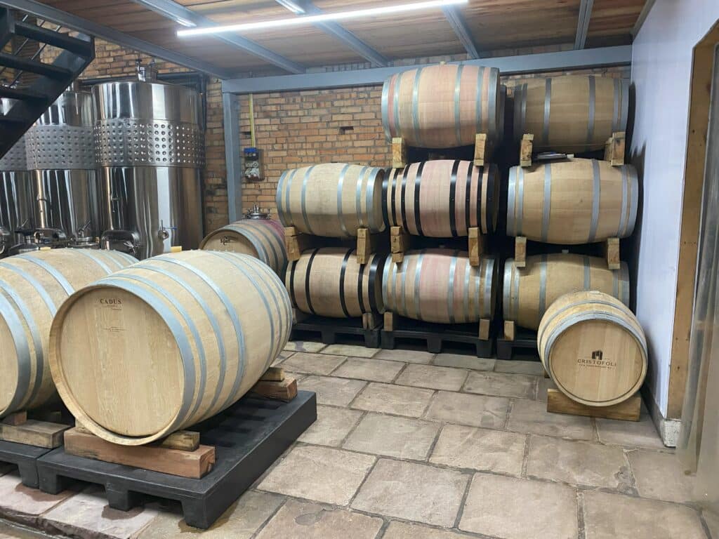 Barris com vinhos Cristofoli, no local de armazenamento da produção da vinícola, sendo possível ver tonéis ao fundo