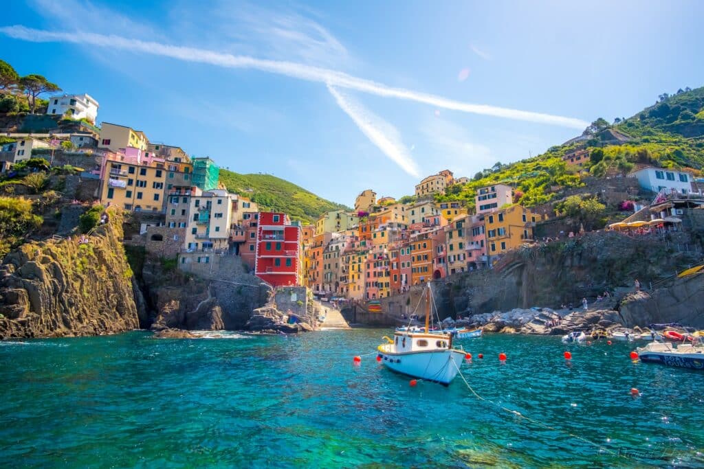 Foto do mar azul com alguns barcos e várias construções coloridas nas pedras que rodeiam o mar e ao fundo uma montanha verde durante o dia, ilustrando post hotéis em Cinque Terre.