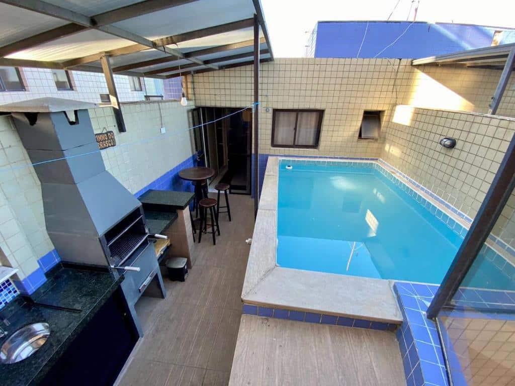 Cobertura de um prédio com piscina privativa azul no lado direito, pia, churrasqueira e pequena mesa redonda com bancos no lado esquerdo, na propriedade do Cobertura Piscina Privativa frente e Vista Mar Centro Mongaguá.