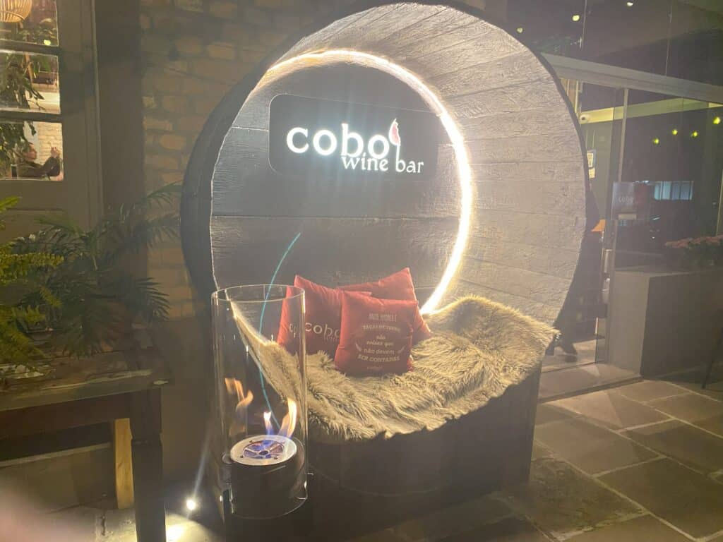 Área para tirar fotos na entrada de um dos restaurantes em Bento Gonçalves, o Cobo Wine Bar, com assento forrado com pele, almofadas vermelhas, e um aquecedor bem em frente