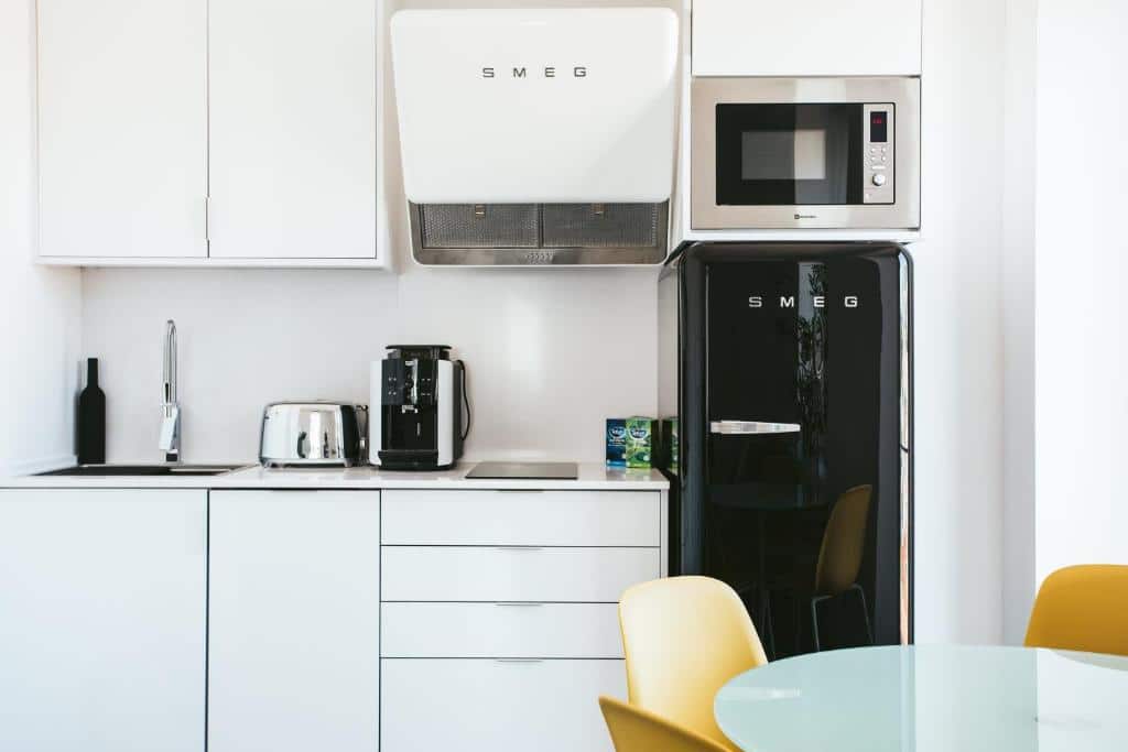 Cozinha do Castello Prime Suites com eletrodomésticos retrô branco ou pretos, armários, uma pequena bancada com torradeira, máquina de café, pia e duas bocas de fogão, para representar hotéis com cozinha em Lisboa