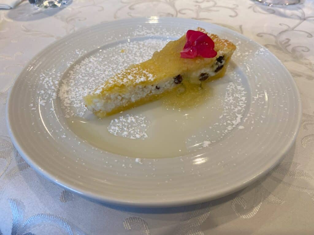 Sobremesa no restaurante da vinícola Cristofoli, em Bento Gonçalves, que consiste numa crostata de ricota com geleia de abacaxi, posicionada sobre um prato branco, polvilhada com açúcar, e enfeitada com uma flor rosa