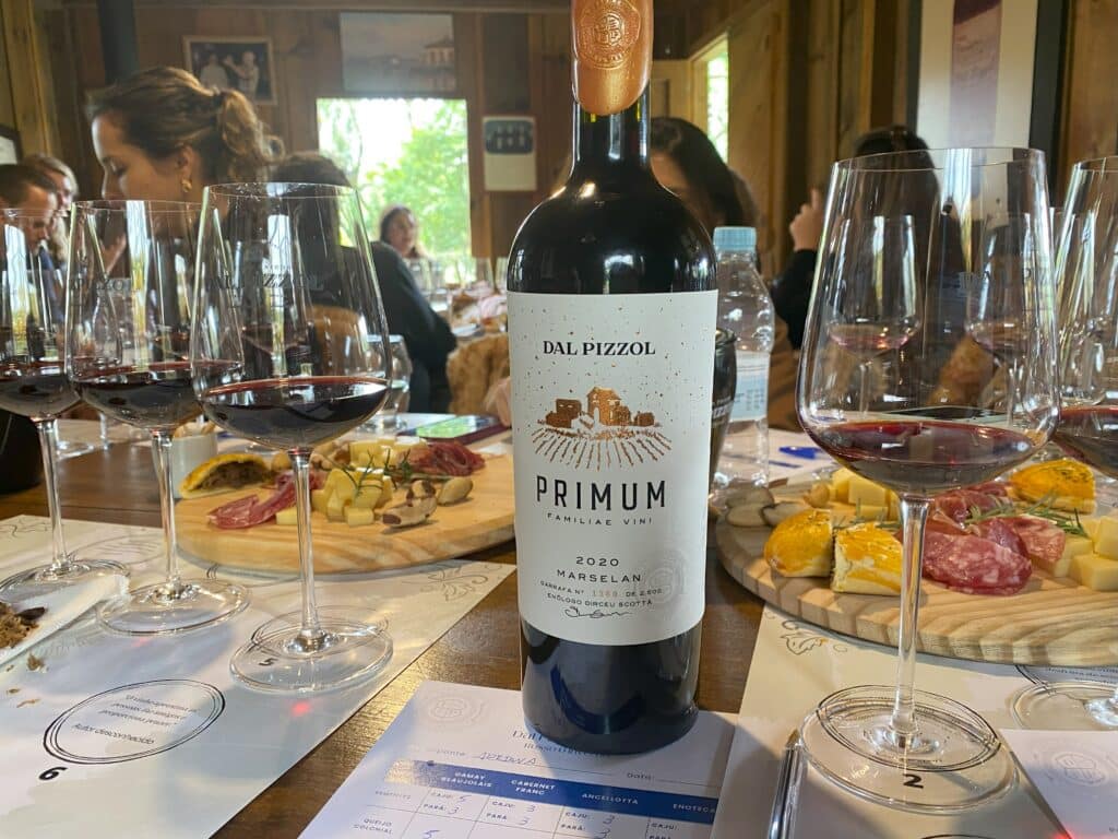 Degustação na Dal Pizzol, uma das vinícolas em Bento Gonçalves, com o rótulo Primum em primeiro plano, da uva Marselan, safra 2020, com taças em volta e tábuas de charcutaria ao fundo
