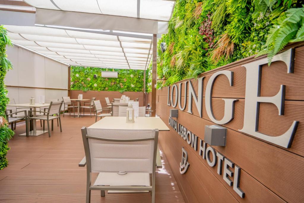 área compartilhada do Dinya Lisbon Hotel & Lounge Bar com mesas e cadeiras, há um teto transparente e plantas nas paredes que cercam o ambiente