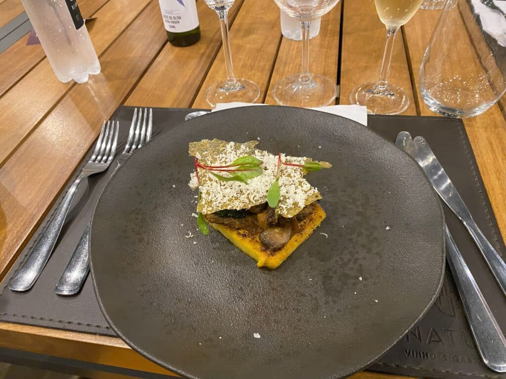 Prato de entrada do restaurante Nature, na vinícola Don Giovanni, com talheres em ambos os lados do prato preto, de cerâmica rústica