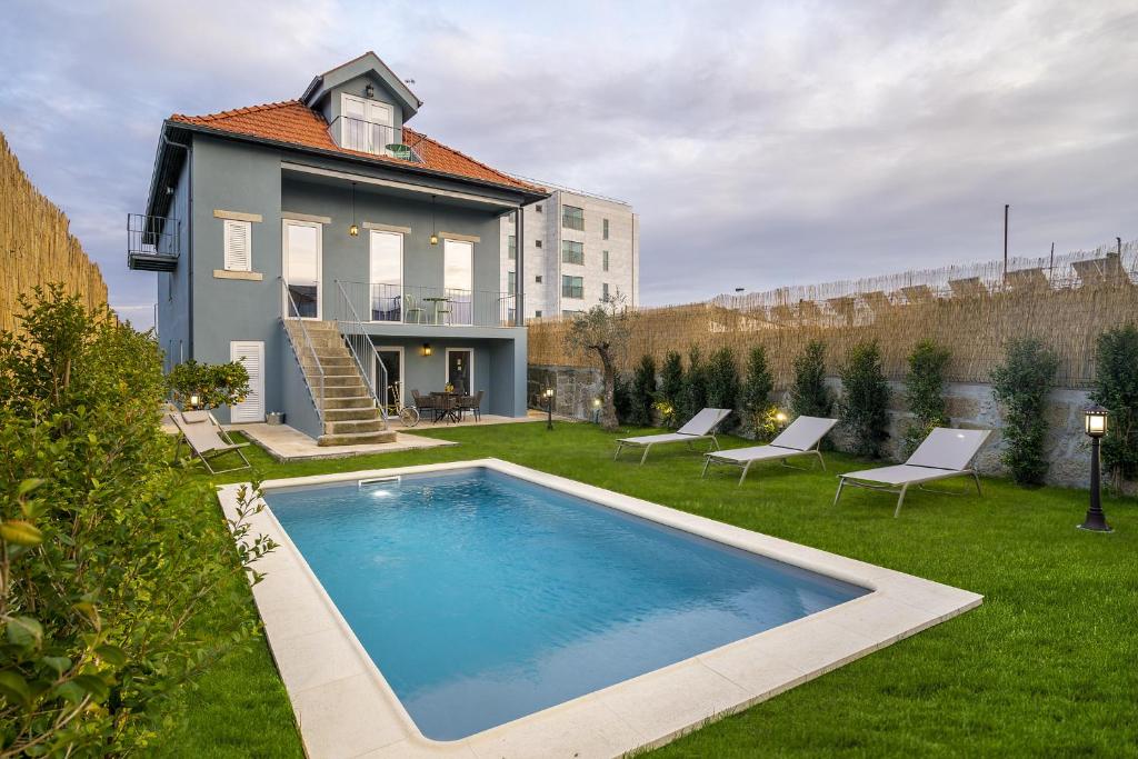 Frente da Douro Prestige Urban Retreat with shared S-Pool & Gym  durante o dia com piscina a frente, do lado direito da imagem três cadeiras brancas e ao fundo a casa com dois andares.