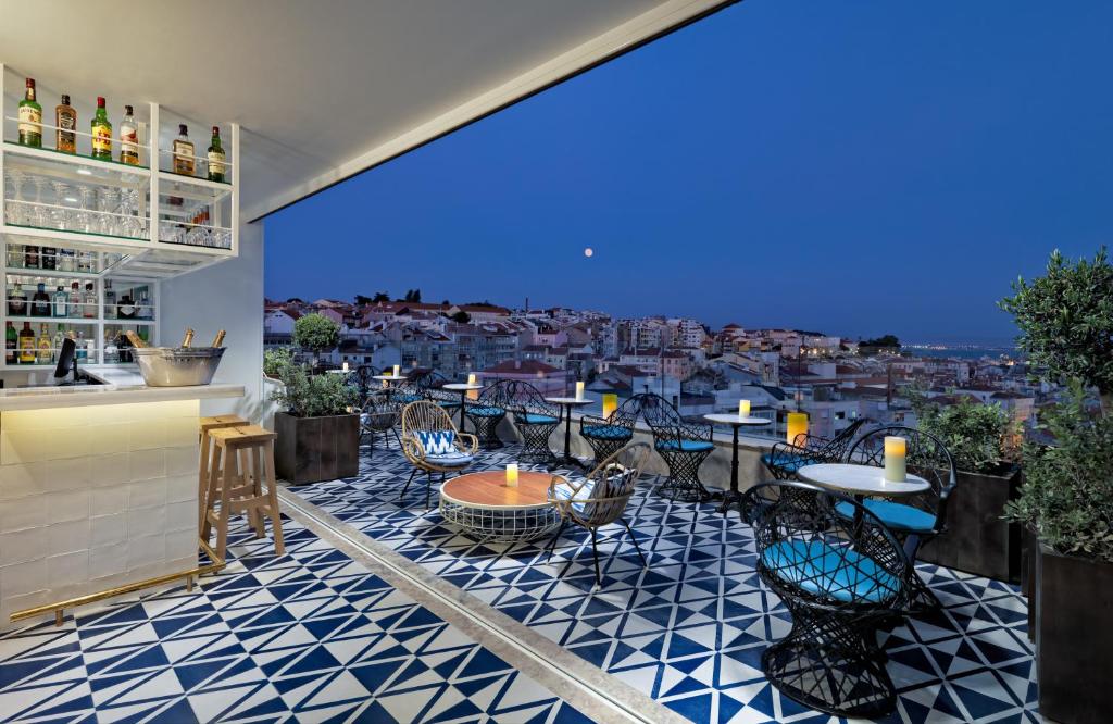 Terraço do H10 Duque de Loule iluminado de noite com uma varanda com mesinhas e cadeiras, tudo nas cores azul e branco, há um pequeno bar do lado esquerdo e alguns vasos de plantas no local, para representar hotéis bem localizados em Lisboa