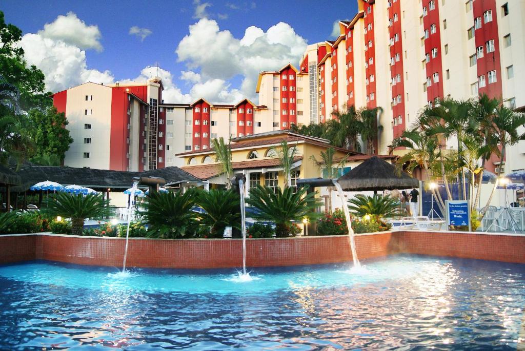 Parte do Hot Springs Hotel - Via Conchal que mostra a piscina azul com três cascatas de água, em volta algumas árvores e ao fundo o hotel, ilustrando Hotéis em Caldas Novas.