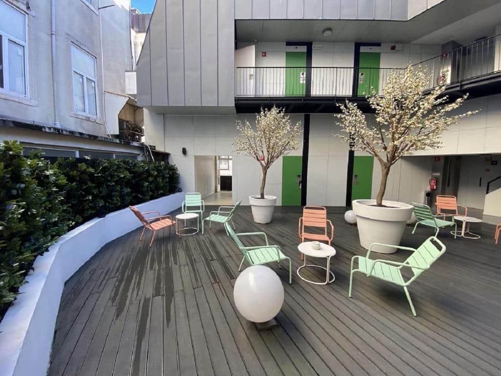 Terraço compartilhado do Hotel Gat Rossio com alguns vasos de plantas, pequena mesinhas com cadeiras coloridas ao redor, o chão é um deck de madeira e o lugar está aos fundos da propriedade