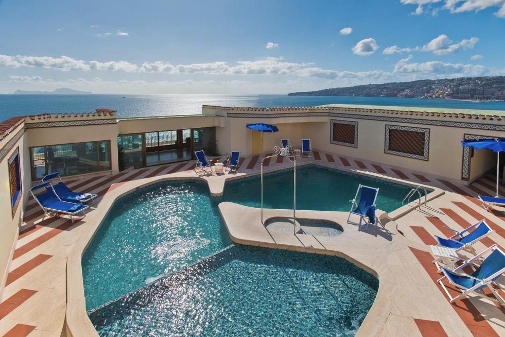 Parte do Hotel Royal Continental que mostra a piscina azul com algumas espreguiçadeiras em volta e ao fundo o mar azul com algumas montanhas, ilustrando post Hotéis em Nápoles.