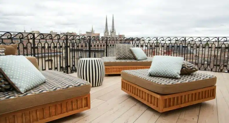 Cobertura do Hôtel Singulier Bordeaux. Existem três poltronas em formato quadrado e distribuidas em formato de roda. Ao fundo está a vista da catedral e da cidade. Representa o post de hotéis em Bourdeaux.