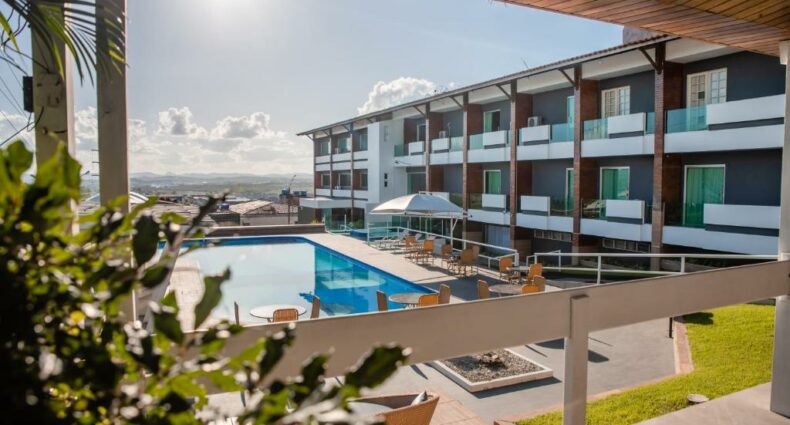 Piscina azul a esquerda, cadeiras amarelas a direita e quartos de hotel com varanda também a direita visto de uma varanda. Imagem para ilustrar o post hotéis em Caruaru.