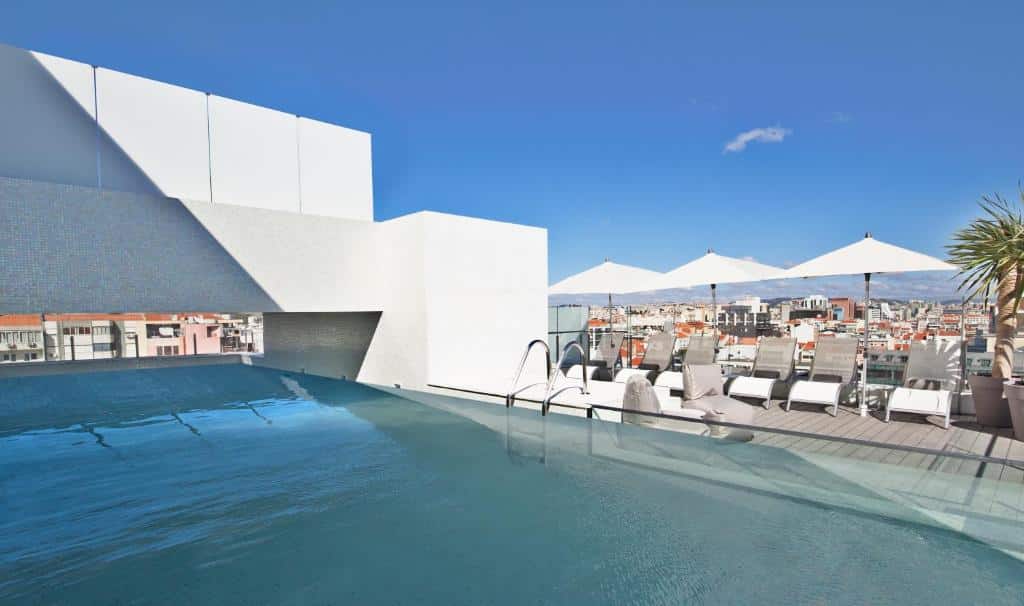 Piscina na cobertura do  Hotel White Lisboa com espreguiçadeiras brancas e guarda-sóis no deck ao redor, para representar hotéis com piscina em Lisboa
