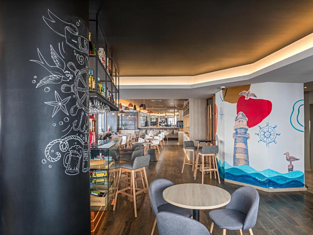 Área de refeições do Hotel Ibis Styles Lisboa Liberdade com mesas redondas, cadeiras estofadas em cinza, paredes com desenhos pintados que remetem ao mar