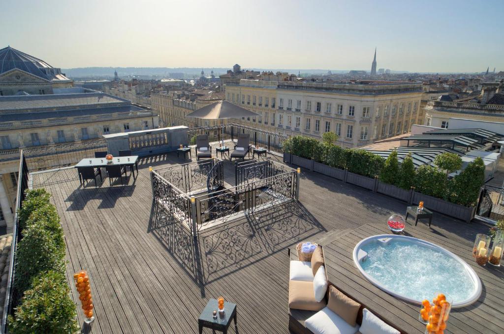 Terraço do InterContinental Bordeaux Le Grand Hotel, an IHG Hotel. No canto direito está um ofurô e algumas almofadas ao redor para sentar. No meio está a escada cercada, que leva até a parte de baixo. Ao lado esquerdo estão uma mesa, cadeiras e duas espreguiçadeiras. Ao redor há uma vista da cidade.