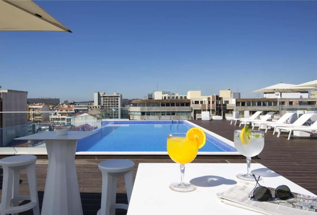 Piscina na cobertura do Jupiter Lisboa Hotel, com um deck espaçoso com espreguiçadeiras brancas e guarda-sóis, para representar hotéis em Lisboa