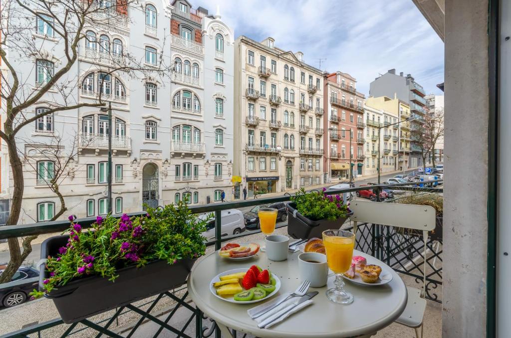 Varanda de um dos quartos do LX51 Studios & Suites – Lisbon center com vista para uma rua com prédios antigos, na varanda há uma mesa com um café da manhã sob ela, para representar hotéis baratos em Lisboa