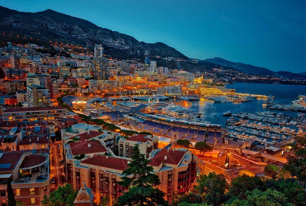 Cidade de Monte Carlo, o mar no fundo no lado direito. No lado esquerdo a cidade. Um monte de prédios iluminados, ao entardecer.