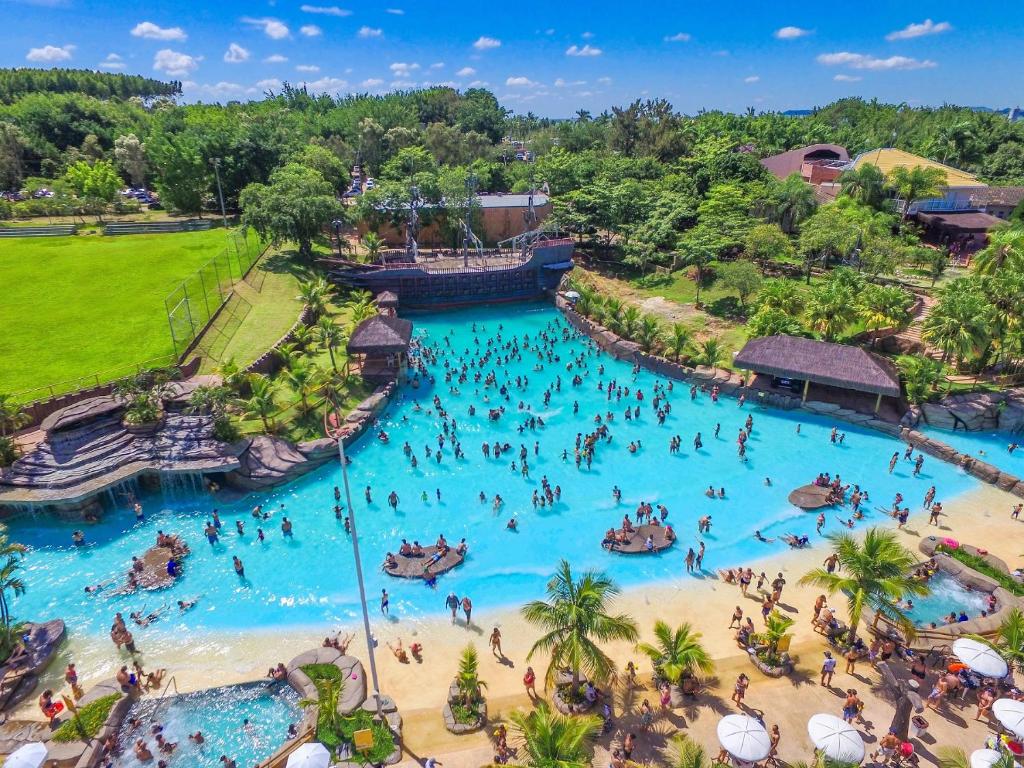 Vista aérea do Thermas Water Park em Águas de São Pedro com várias pessoas dentro da piscina. A água é azul cristalina e há muito vede ao redor.
