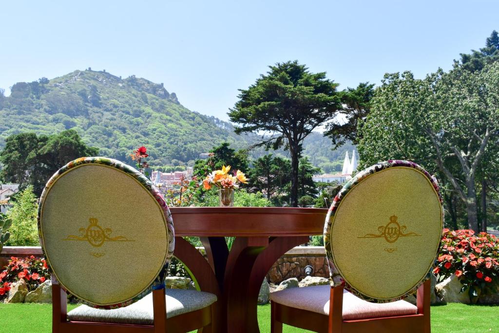 Jardim do Sintra Marmoris Palace com uma mesa redonda de madeira e duas cadeiras estofadas de frente para as flores, árvores e montanhas, para representar hotéis românticos perto de Lisboa