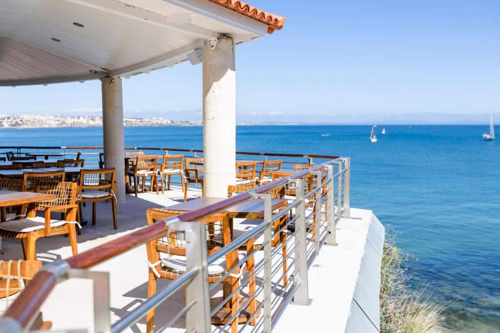 Área de refeições do The Albatroz Hotel, trata-se de um local aberto com vista direta para o mar, há mesas e cadeiras de madeira, para representar hotéis românticos perto de Lisboa