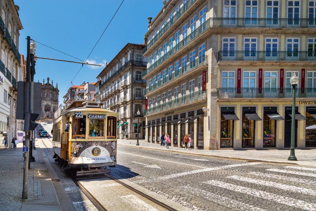 Rua no Porto com edifícios em volta e um bondinho do lado esquerdo da imagem durante o dia. Representa onde ficar no Porto.