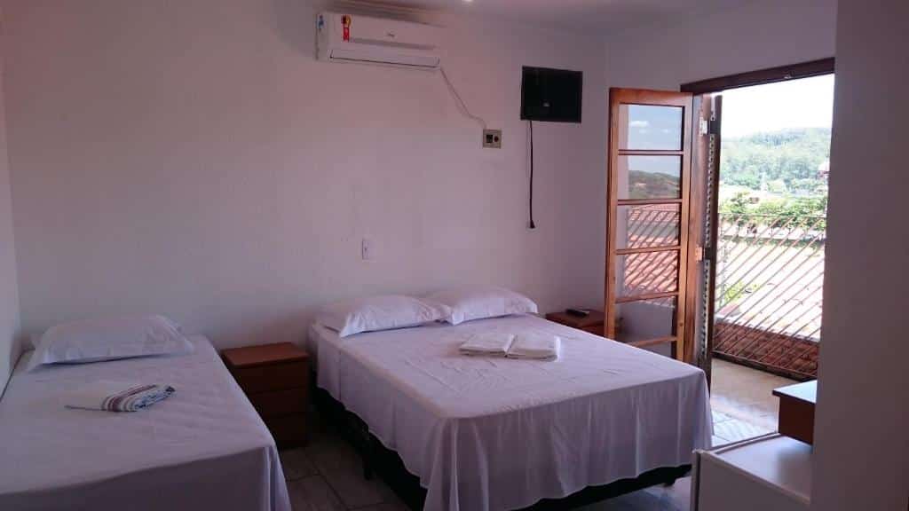 Foto do quarto na Pousada Casablanca ilustrando o post sobre pousadas em Águas de São Pedro. O quarto é espaçoso, possui uma cama de casal do lado de uma porta que dá passagem para a varanda, e outra cama de solteiro encostada na parede.