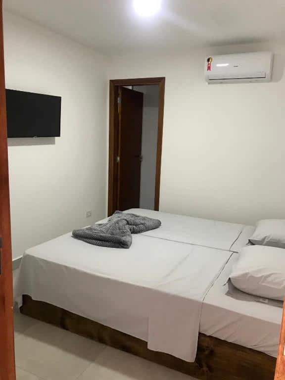 Imagem de um quarto na Pousada Vila Barboza para representar o post sobre pousadas em Águas de São Pedro. Vemos uma cama de casal, unida por duas camas de solteiro, com travesseiros e lençóis brancos. Uma televisão está fixa na parede.