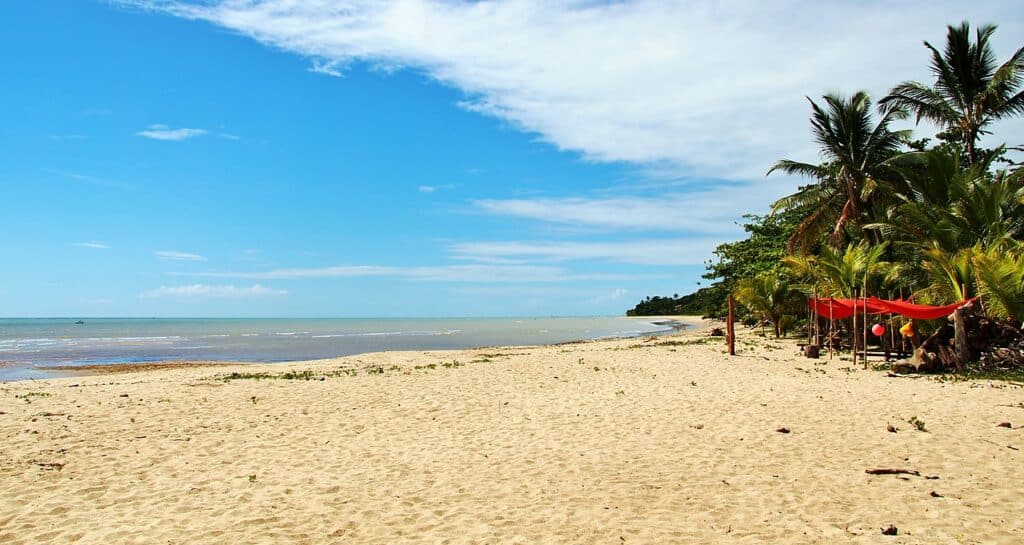 Praia do Peixe Grande, em Cumuruxatiba, na Bahia. Areia da praia na frente, no lado direito árvores e palmeiras. No lado esquerdo o mar. Foto para ilustrar post de pousadas em Cumuruxatiba (BA).