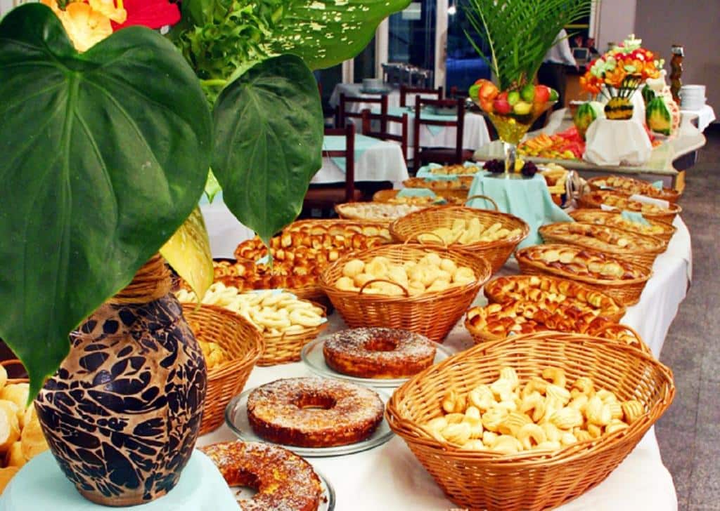 Imagem do café da manhã do Prive Thermas - OFICIAL com alguns bolos, pães em cestas e algumas plantas em vasos de decoração, ilustrando post Hotéis em Caldas Novas.