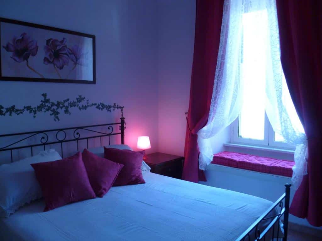 quarto do Holiday Home Il Sogno A San Pietro, um airbnb em Roma, com cama de casal, mesinha e luminária de ambos os lados almofadas e e cortinas combinam no tom de vermelho, e há um aquecedor embaixo da janela