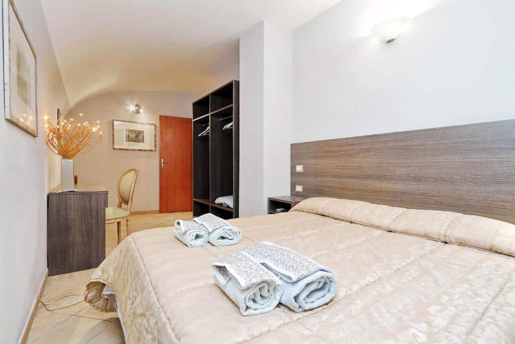 quarto do Monti House Rome, um airbnb em Roma, cama bem grande, toalhas em cima, mesinha de cabeceira de ambos os lados, guarda-roupa aberto e, em frente, mesa com cadeira
