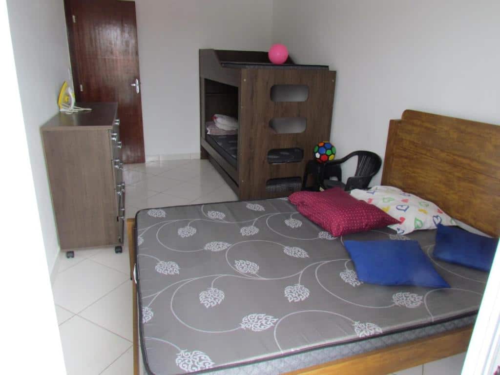 Quarto com beliche encostada na parede direita, cama de casal também na direita e pequena cômoda de madeira na esquerda. Imagem para ilustrar o post pousadas em Mongaguá.