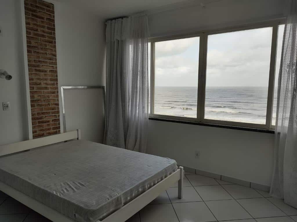Quarto do Apto frente ao mar. Uma cama de casal no lado esquerdo e no lado direito uma janela grande com bastante luz natural e vista para o mar.