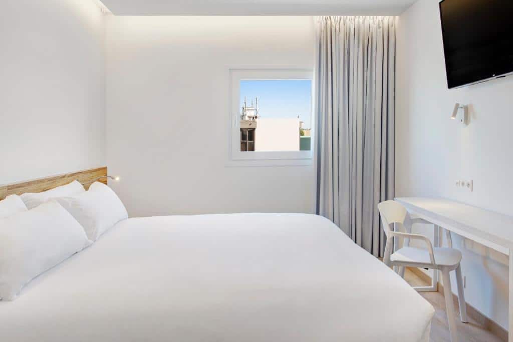 Quarto do B&B HOTEL Porto Expo Aeroporto com cama de casal do lado esquerdo da imagem, em frente a cama uma mesa com cadeira e acima uma TV presa na parede. Representa hotéis perto do aeroporto do Porto.