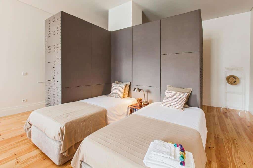 Quarto do bnapartments Loftpuzzle com duas camas de solteiro do lado direito com uma cômoda de madeira no meio delas com luminária. Representa airbnb no Porto.