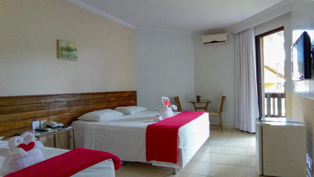 Quarto do Caldas Park & Hotel XPTO Turismo com duas camas do lado esquerdo da imagem, sendo uma cama no lado esquerdo com uma mesa de vidro com telefone do lado e do outro lado uma cama de casal. Do lado da cama de casal uma mesa redonda com duas cadeiras e em frente as camas um frigobar e uma TV presa na parede. Representa resorts em Caldas Novas.