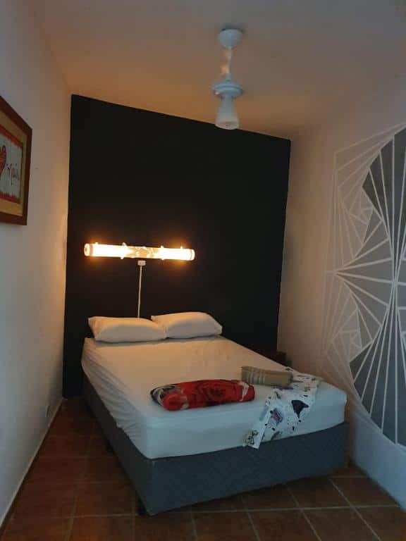 Quarto pequeno com cama de casal levemente inclinada para a direita, parede preta atrás da cama com frase não legível em luz de led. Imagem para ilustrar o post pousadas em Mongaguá.