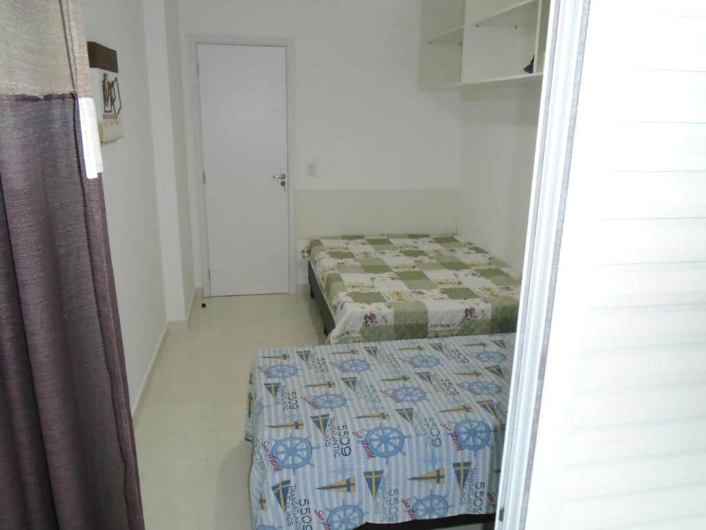Quarto com paredes brancas, cama de casal ao lado da porta na entrada do quarto e cama de solteiro encostada na parede aos fundos do quarto. Imagem para ilustrar o post pousadas em Mongaguá.