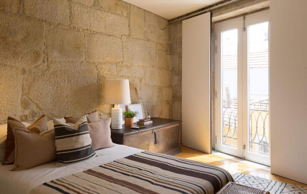Quarto da Casa Castanha com cama de casal do lado esquerdo com uma cômoda de madeira do lado direito com luminária. Representa airbnb no Porto.