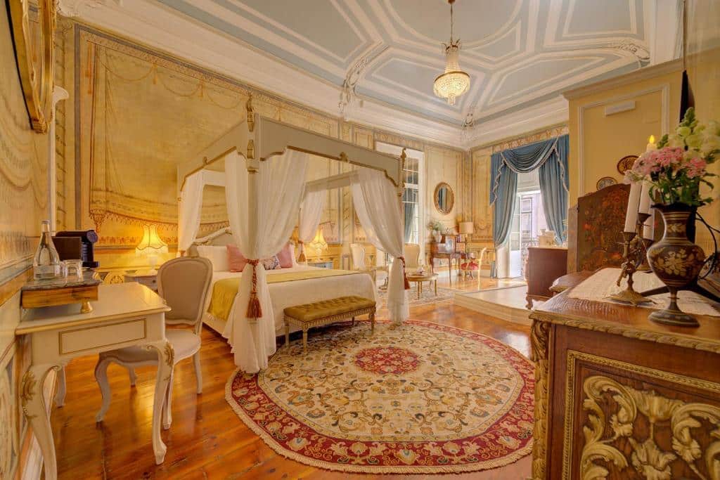 Quarto de luxo com decoração inspirada na realeza de Portugal, com cama cama ampla, lustre, itens de decoração dourados e bom espaço interno no Palácio das Especiarias, para representar hotéis românticos em Lisboa