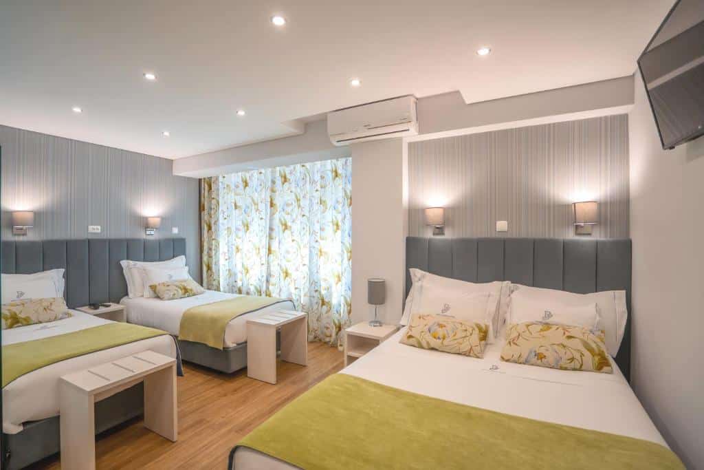 Quarto do Dinya Lisbon Hotel & Lounge Bar com uma cama de casal, duas de solteiro, uma janela com cortinas, uma televisão e um ar-condicionado de teto, para representar hotéis para família em Lisboa