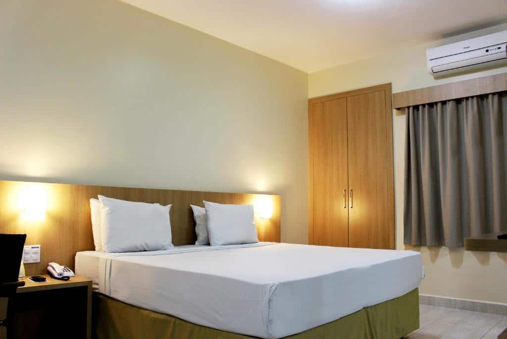 Quarto do Hot Springs Hotel - Via Conchal com uma cama de casal com móveis de madeira, como uma mesinha do lado da cama e do outro lado um guarda-roupa e também uma cortina ao lado do guarda-roupa.