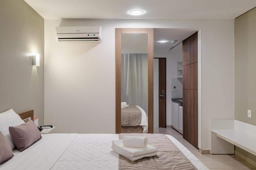 Quarto do Citi Hotel Residence Caruaru. A cama está encostada no lado esquerdo do quarto, no lado direito há uma grande prateleira e ao fundo há um espelho e uma entrada para uma pequena cozinha. Imagem para ilustrar o post hotéis em Caruaru.