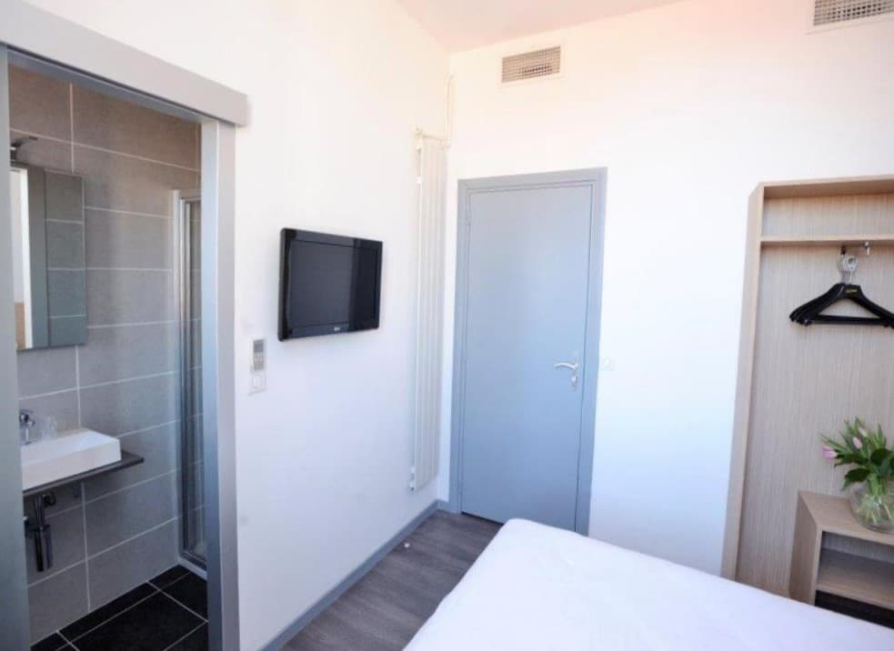 Quarto do Hôtel de France. De frente pra cama a porta do banheiro e uma televisão. No lado direito a porta do quarto e um guarda-roupa.